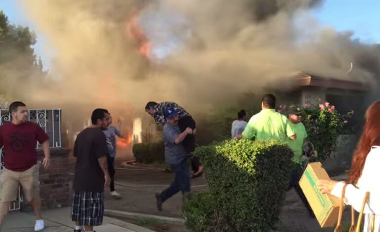 An older man is carried from a flaming house.