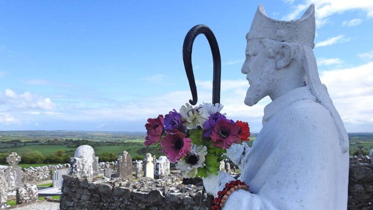 Statue of St. Patrick with flowers and facts surrounded by the Irish countryside