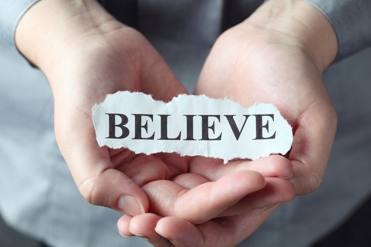 The lie in believe - woman holding a scrap of paper with the word "believe"