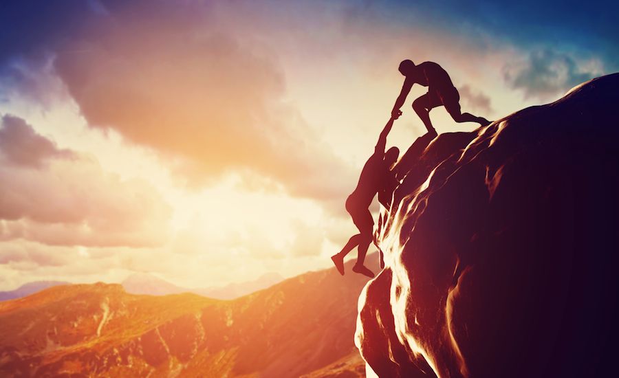 Man helping another man up a cliff. Shutterstock.