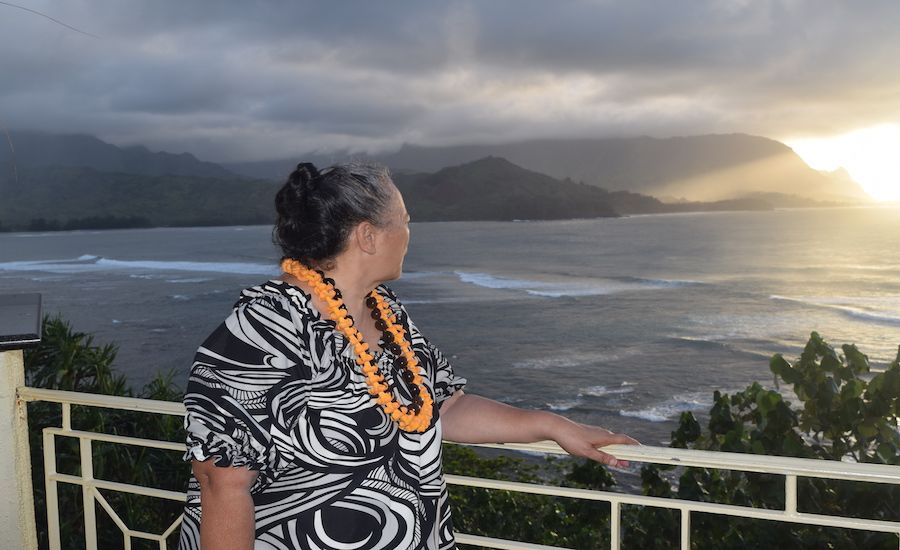 A Hawaiian woman stands on the balcony of the St. Regis Kauai hotel at sunset