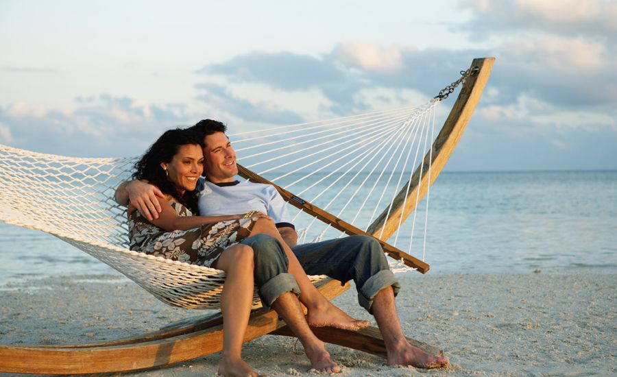 a man and a woman cuddle on a hammock on the beach on a nice day