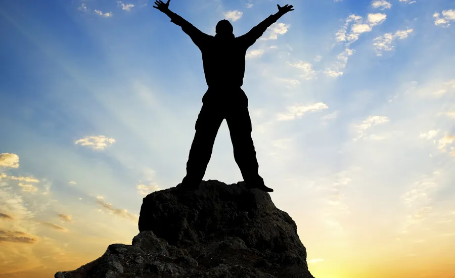 person in shadow stands on top of a rock before dawn