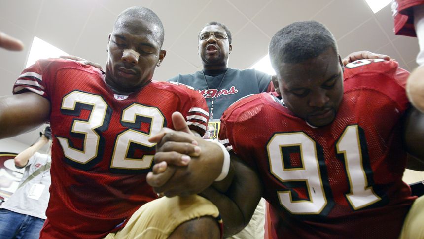 Smith prays with Kevan Barlow (left) and Anthony Adams in the locker room before a 2005 home game against the Indianapolis Colts.