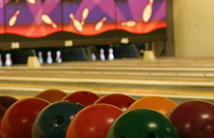 bowling balls lined up on a rack at bowling alley with lanes and pins in the background