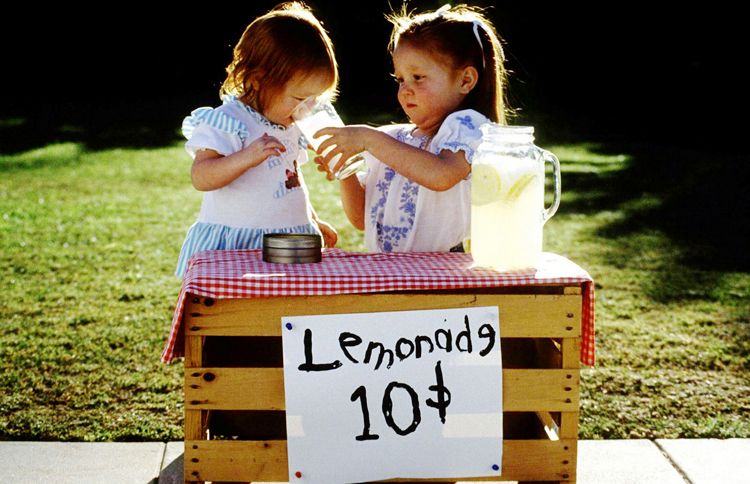 Two adorable little girls operate a lemonade stand on a warm summer day.