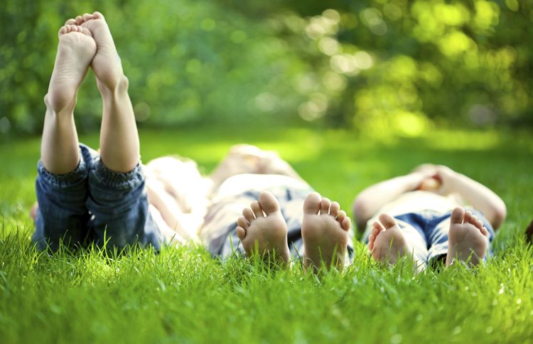 Barefoot children lie on their backs in the grass on warm, sunny summer day.