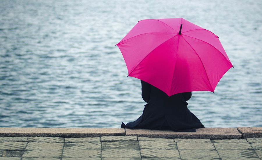 A woman sits at a river's edge holding a pink umbrella preparing for a storm. Prepare for the storms of life with these tips