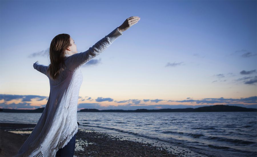 a woman with outstretched hands looks out over water willing to be obedient