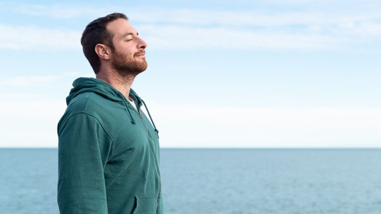 Man near the ocean closing his eyes and thinking about how to be more thankful