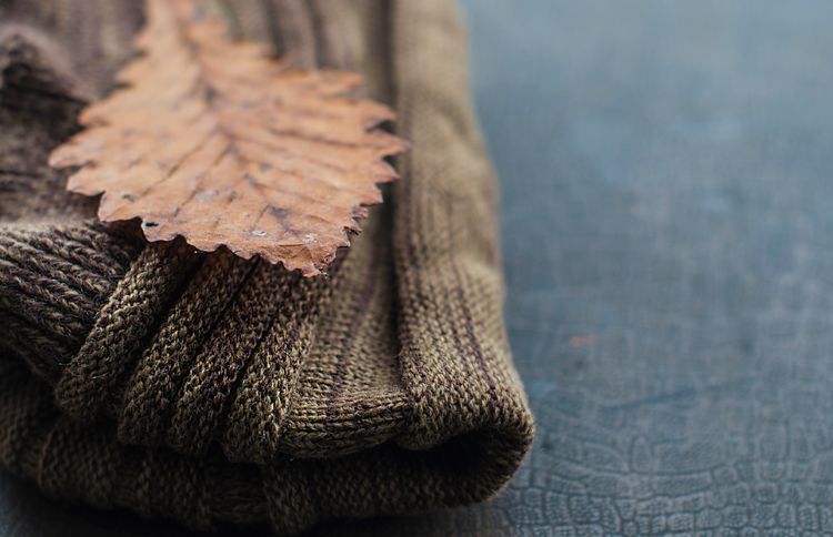 Guideposts: A folded woolen sweater on a shelf, with a single autumn leaf resting on it.