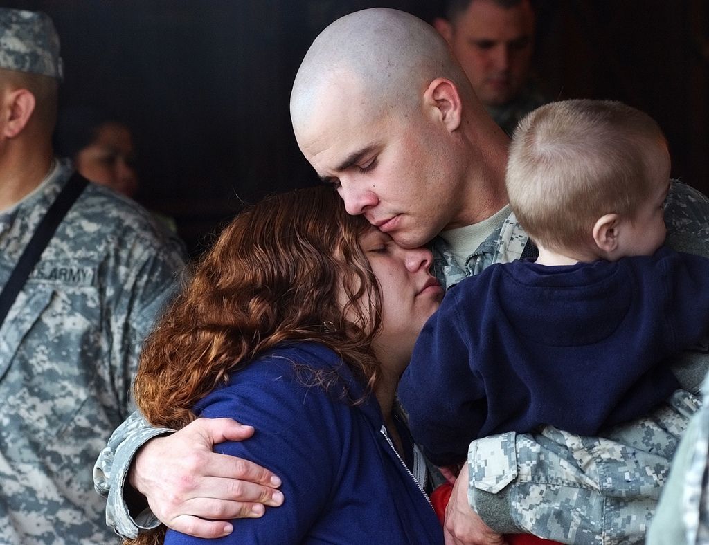Guideposts: A soldier in fatigues hugs his wife and child.