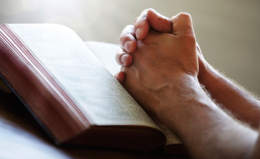 Guideposts: A man's hands, clasped in prayer, rest on the pages of an open Bible