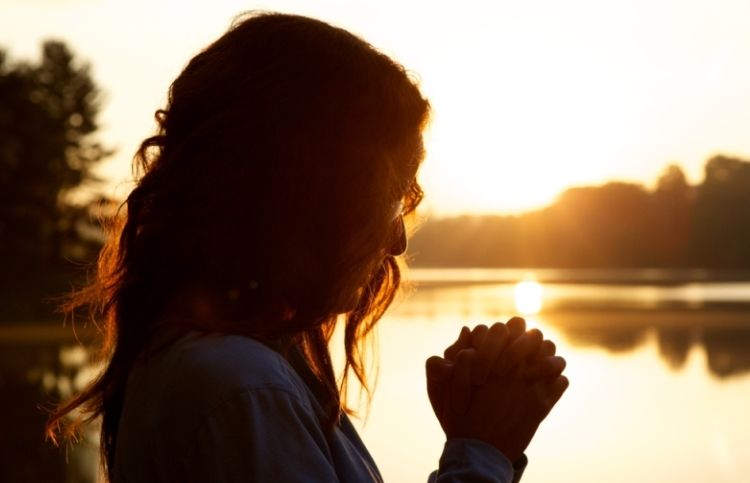 woman praying at a beautiful lake: tips to help you remember to pray.