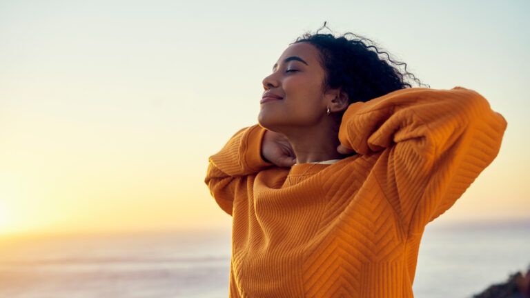A woman in an orange sweater with her eyes closed looking happy with gratitude quotes