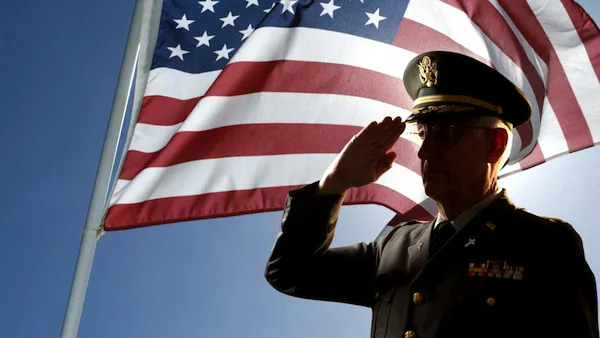 A veteran salutes in front of a flag and says Veterans Day prayers