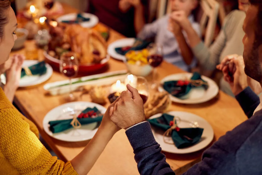 Close-up of family holding hands and saying Christmas quotes before dinner