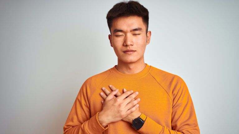 Man in an orange sweater with his hand over his heart asking for forgiveness in the new year