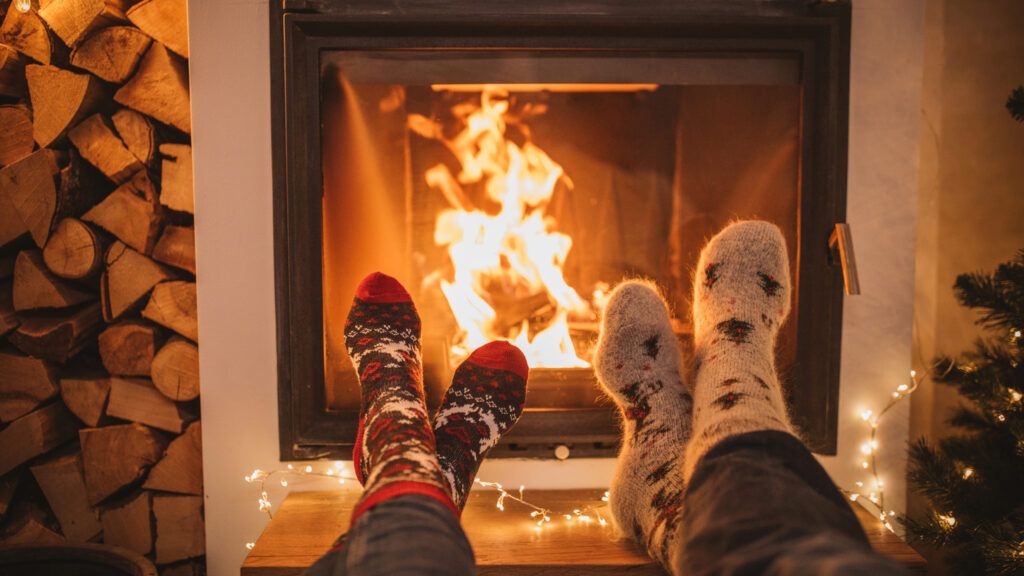 Two people in Christmas socks warming their feet in front of the fireplace while reading Christmas quotes