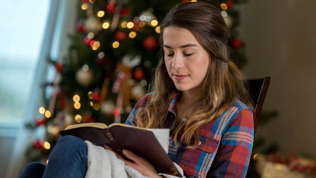 Woman in front of a Christmas tree reading a Bible and saying a Christmas prayer