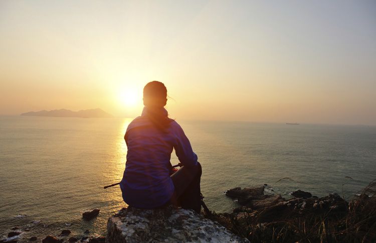 Woman sitting on a cliff staring at the sun with a new year bible verse