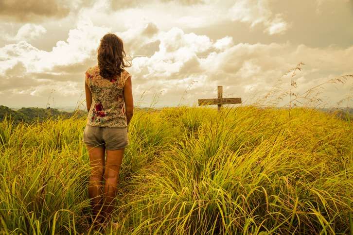 Guideposts: A woman gazes across a sunlight field at a cross.