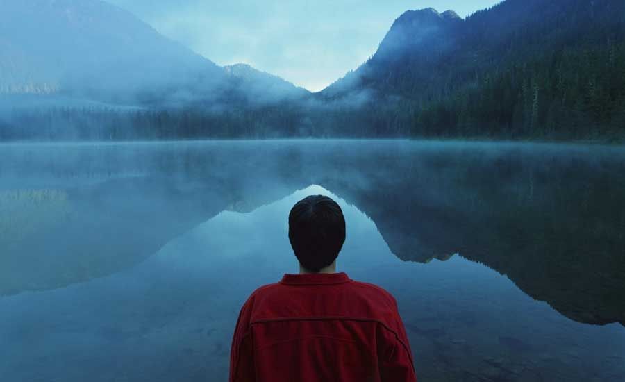 Guideposts: A young man stands gazing out at a fog-covered lake surrounded by mountains