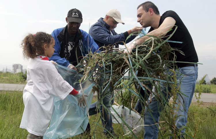 Guideposts: A young girl holds a trash bag open while a group of volunteers places tree trimmings in it.