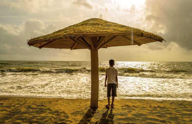 Guideposts: A young boy watches the sunset over the ocean from under a thatch beach umbrella