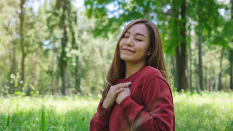 A woman in nature with her hand on her heart feeling God's love through quotes