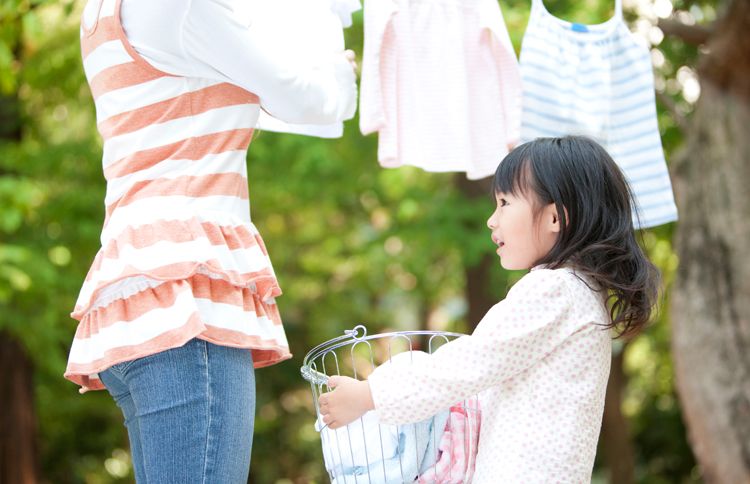 Guideposts: A young girl holds the laundry basket as her mother hangs the wash from the line