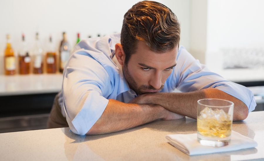 A man struggles to resist drinking a glass of alcohol that rests in front of him