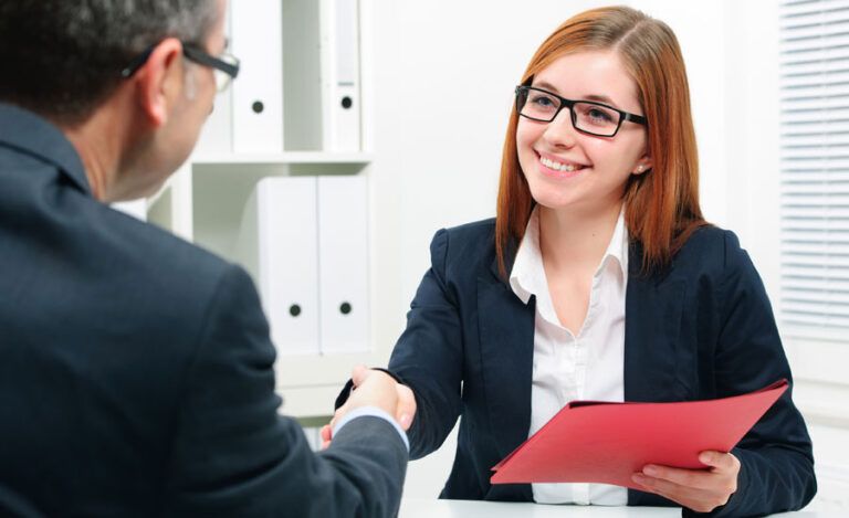A smiling woman shakes a man's hand following a successful job interview.
