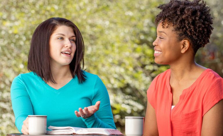 Two women smile as they chat over coffee, an open Bible between them