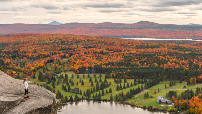 Woman looking at Lyster lake with forest of Quebec and Vermont seen from the Mount Pinacle in Coaticook during autumn. Woman looking at lake and forest during autumn.