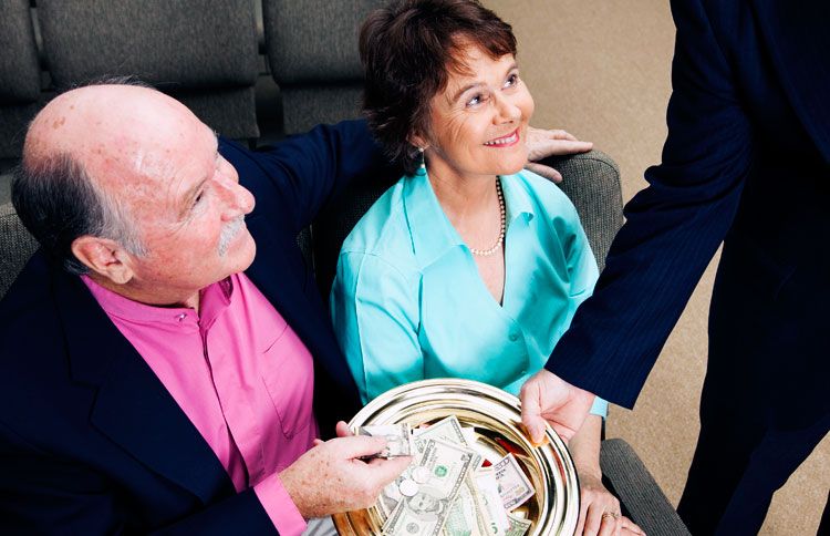 A smiling married couple places a donation in a church offering plate