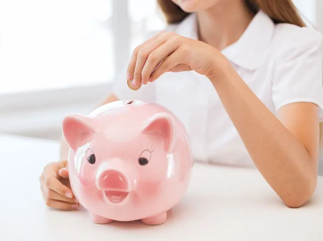 A woman places a coin into a pink piggy bank