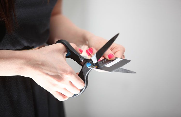 A woman uses scissors to cut a credit card in half.