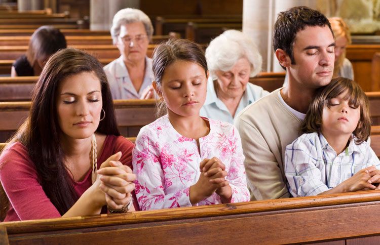 A family bows its heads in prayer in church