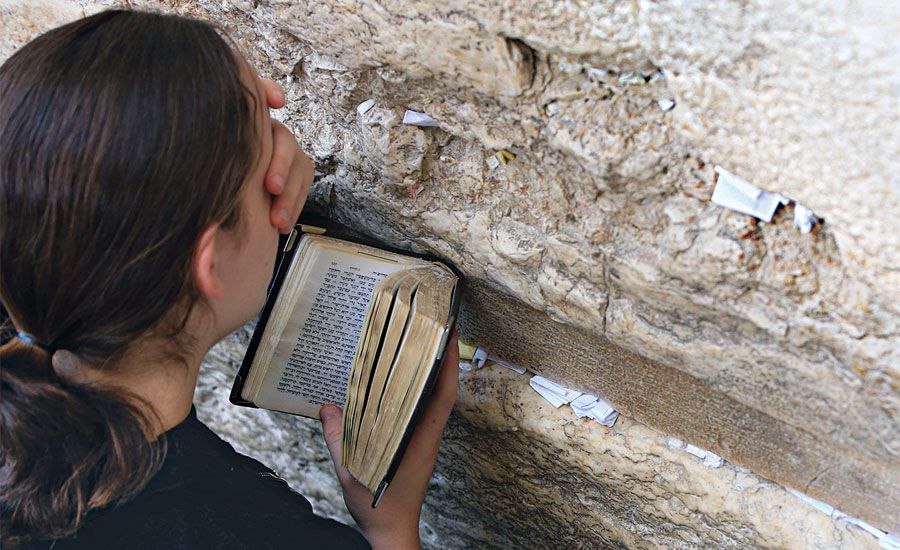 A young woman prays at the Wailing Wall, an open prayer book in her hand