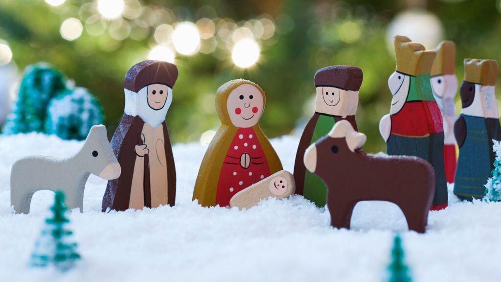 A wooden nativity set, with a colorful Christmas tree behind it