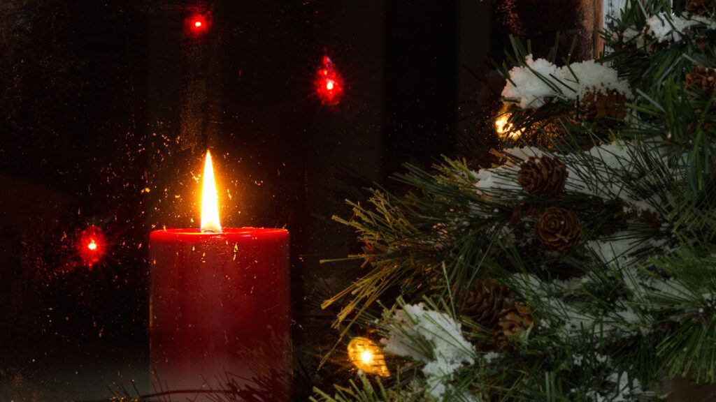 A red candle as prayers for the suffering in the window next to a christmas tree