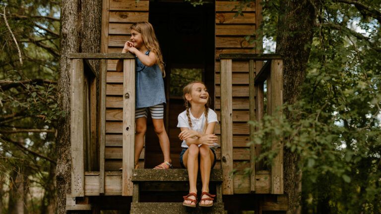 Two girls sitting in a treehouse.