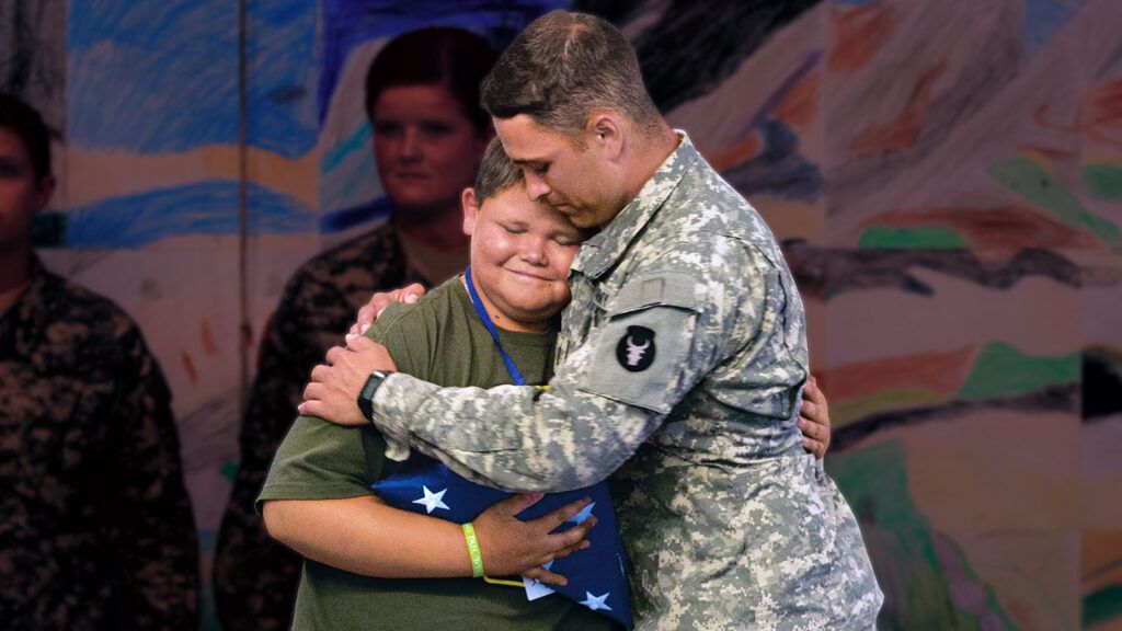 a 9-year-old boy in a green shirt smiles as he gets a hug from a man in a green U.S. military uniform
