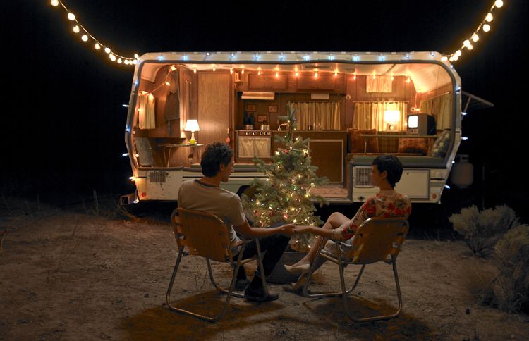 A couple sits outside their travel trailer, enjoying the small Christmas tree positioned there