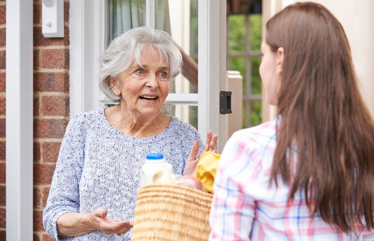 A young woman surprises a senior woman with a bag of groceries