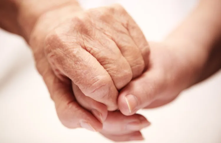 An older woman's hand is comforted by the clasp of a young woman's hand