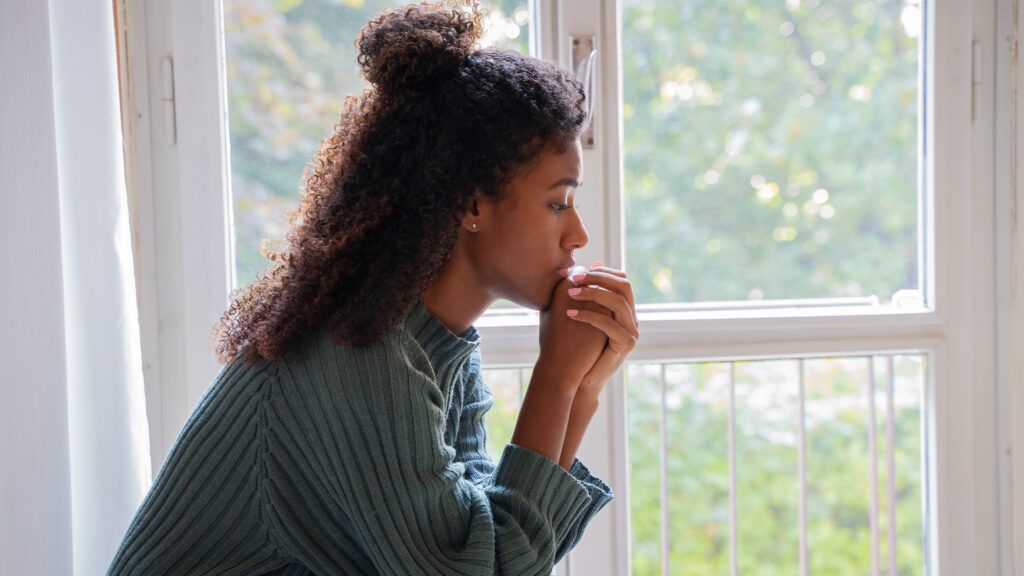 Woman looking sad in a sweater by the window says winter prayers