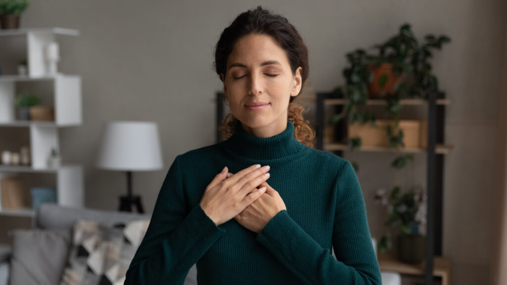 Woman with closed eyes with her hands on her heart says a winter prayer