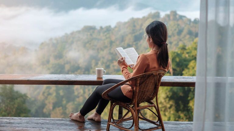 Woman sits by a view reading about spiritual spring cleaning